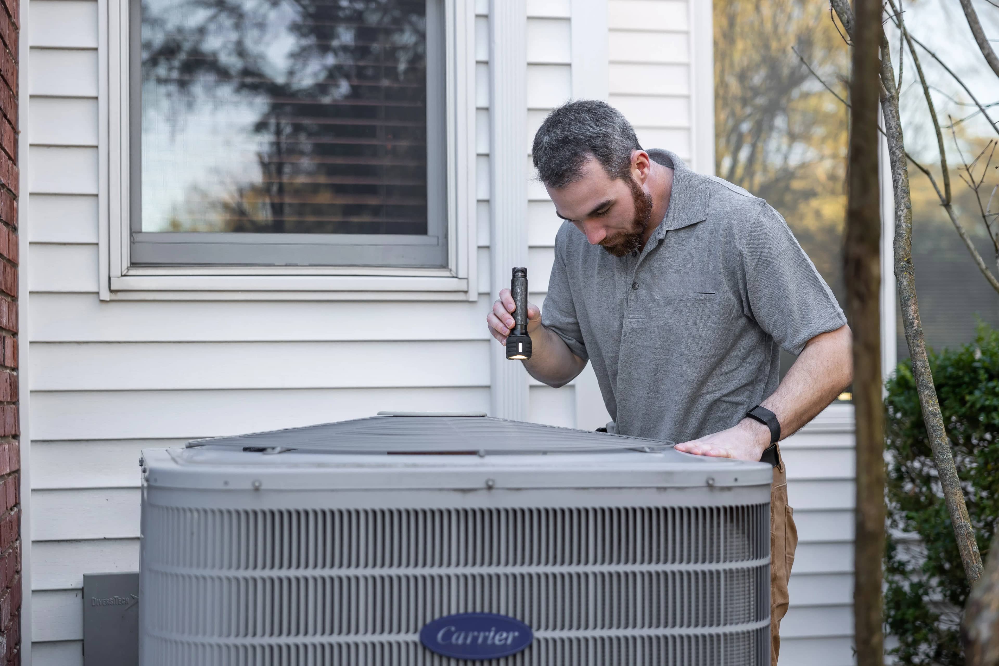 HVAC technician checking an outdoor condenser beside a house